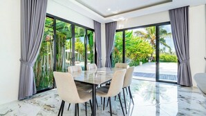 A modern dining area with a glass table and chairs, large windows with curtains, and a view of greenery outside. - Serene 3BR Villa w Huge Pool+Garden • Central Ubud (Sukawati)