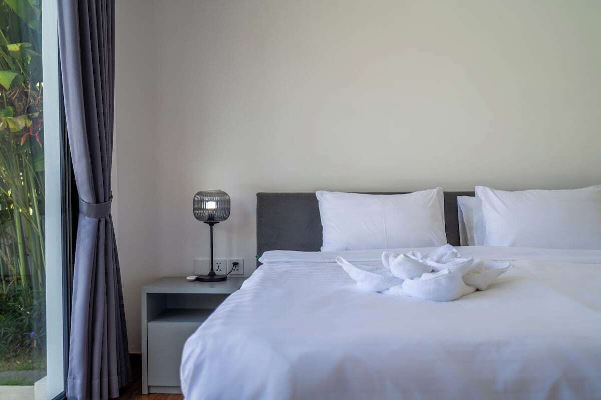 A hotel room with a bed, a bedside table with a lamp, and a window with curtains.