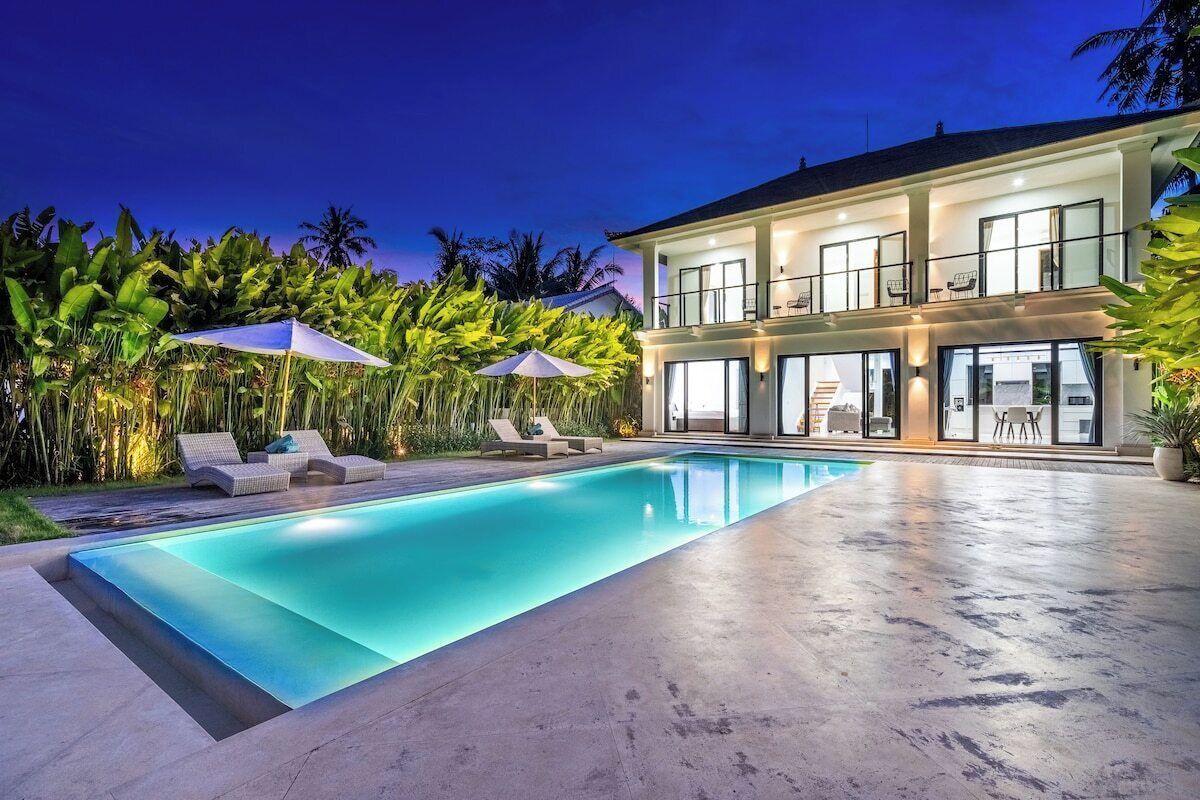 A modern two-story house with a swimming pool, outdoor seating, and lush tropical vegetation.