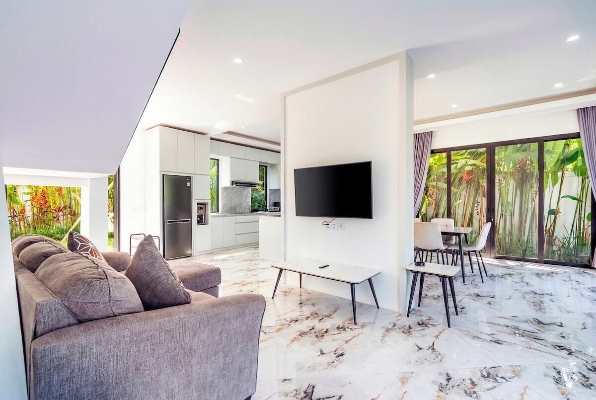 A modern living room with a sofa, a flat-screen TV, and a dining area with chairs and a table.