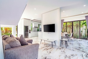 A modern living room with a sofa, a flat-screen TV, and a dining area with chairs and a table. - Serene 3BR Villa w Huge Pool+Garden • Central Ubud (Sukawati)