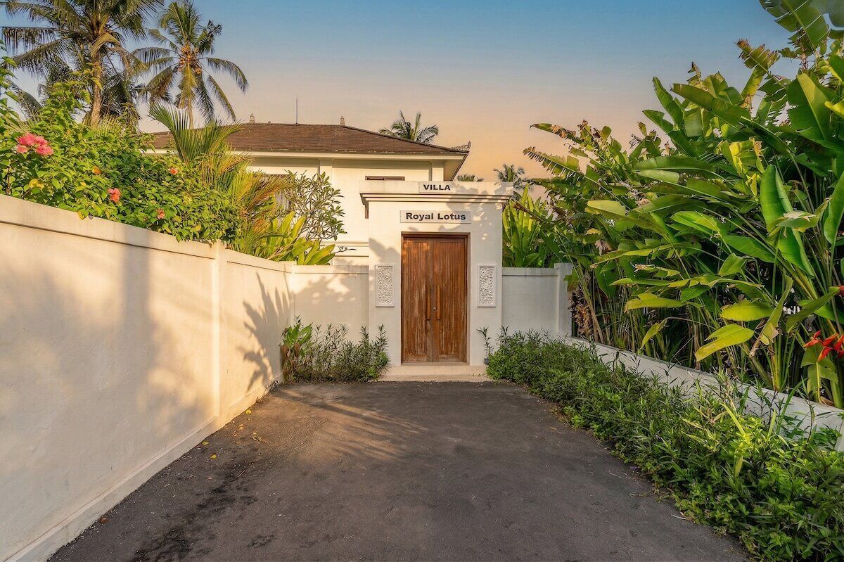 A villa entrance with a wooden door, a sign reading 'Royal Lotus,' and lush tropical vegetation.