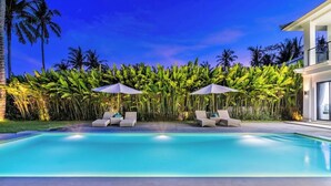 A swimming pool with lounge chairs and umbrellas, surrounded by lush greenery and palm trees. - Serene 3BR Villa w Huge Pool+Garden • Central Ubud (Sukawati)