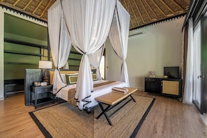 A room with a bed under a canopy, a bedside table with a lamp, a small table with a towel, and a television on a cabinet. - Peaceful 1BR Villa in Lush Ubud w Pool & Garden (Gianyar Regency)