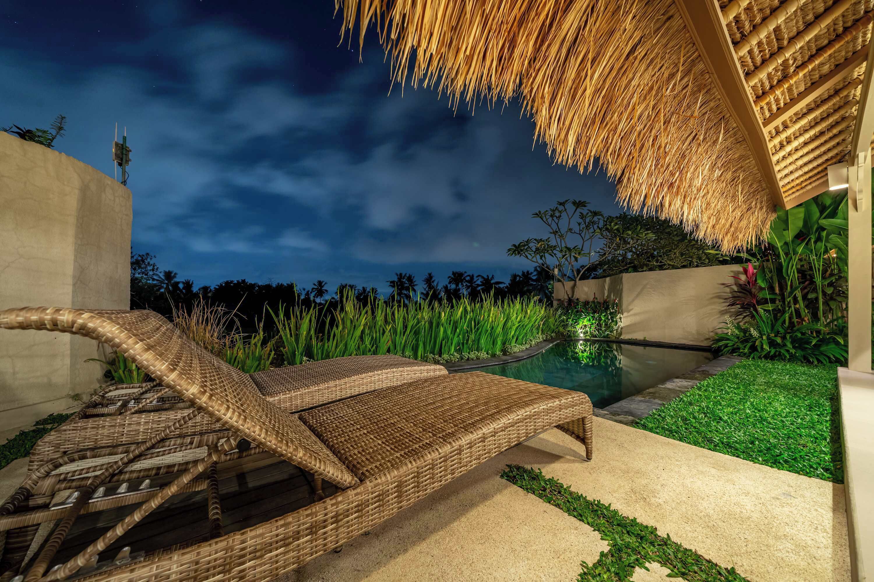 A poolside area with a thatched roof, wicker lounge chairs, and a well-maintained garden.