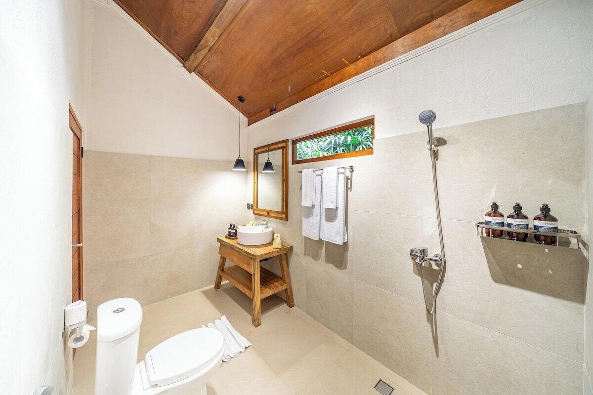 A bathroom with a wooden vanity, a toilet, a shower, and a mirror.