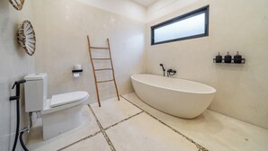 A modern bathroom with a freestanding bathtub, toilet, and a window providing natural light. - Tropical 1BR in Ubud w Pool - Perfect for Couples! (Tampaksiring)