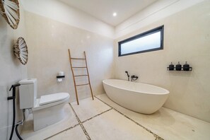 A modern bathroom with a freestanding bathtub, toilet, and a window providing natural light. - Tropical 1BR in Ubud w Pool - Perfect for Couples! (Tampaksiring)