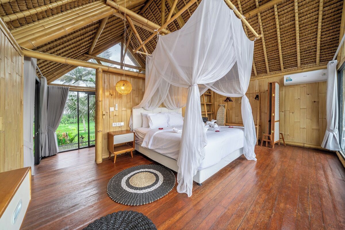 Ein Schlafzimmer mit Himmelsbett, Holzboden und Blick auf Grünfläche.