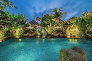 A swimming pool with lounge chairs and umbrellas, surrounded by lush greenery and a clear sky. - Brand New 2BR Boho Stay w Spa & Pool - Ubud's Best (Ubud)