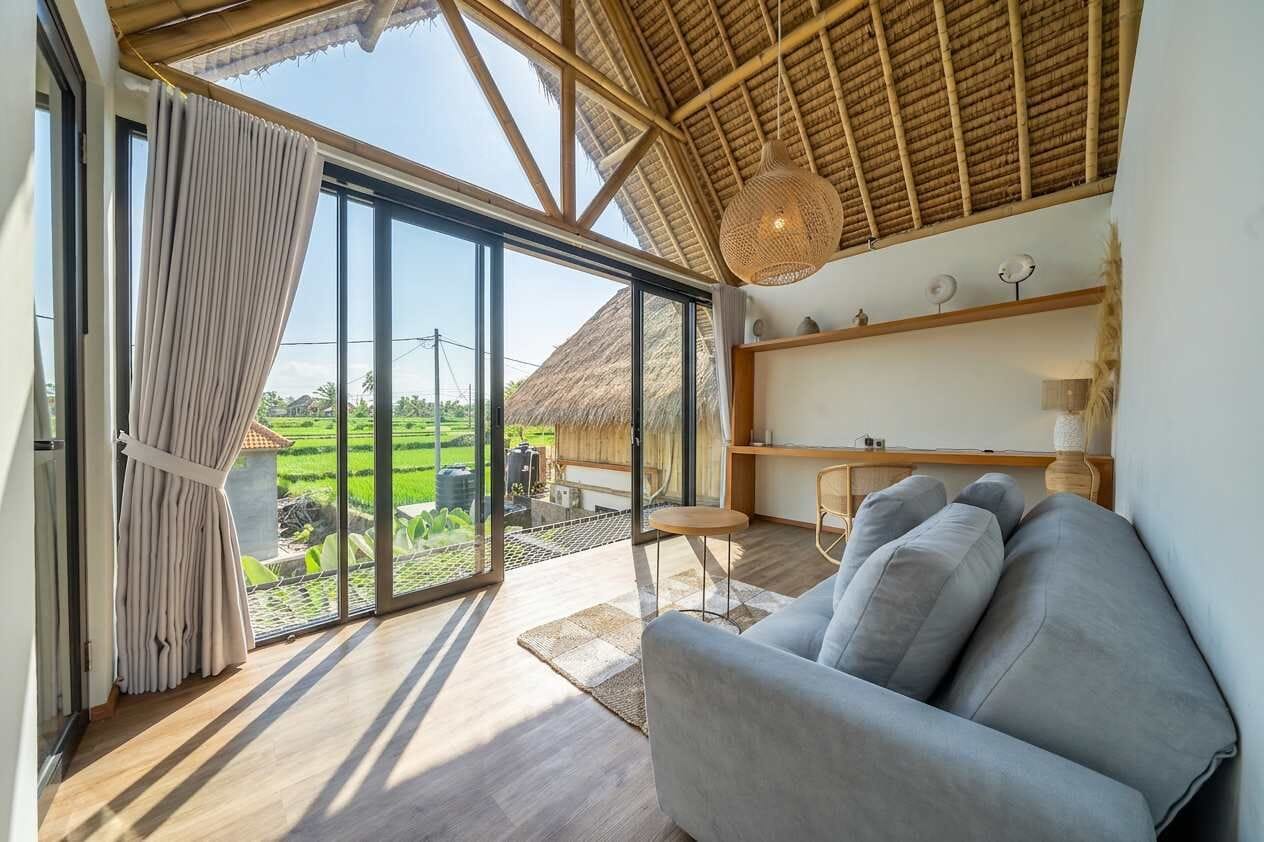 Ein modernes Wohnzimmer mit einem großen Schiebeglasfenster, das auf einen Balkon führt, einer Couch, einem kleinen Tisch und einer Pendelleuchte.