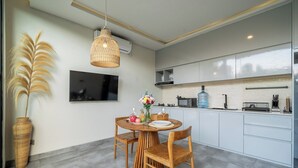 A modern kitchen with white cabinets, a dining table with chairs, a large vase with flowers, and a hanging light fixture. - Brand NEW 1BR Villa+Huge Pool+Jungle View+Top Spot (Gianyar Regency)