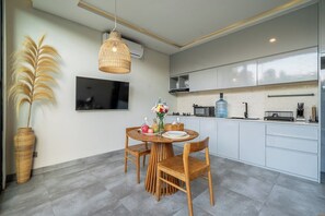 A modern kitchen with white cabinets, a dining table with chairs, a large vase with flowers, and a hanging light fixture. - Brand NEW 1BR Villa+Huge Pool+Jungle View+Top Spot (Gianyar Regency)