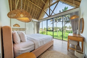 A bedroom with a large bed, a wooden desk, and a view of the outdoors. - Brand NEW 1BR Villa+Huge Pool+Jungle View+Top Spot (Gianyar Regency)