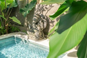 Eine Steinstatue an einem Pool mit klarem Wasser, umgeben von viel Grün.