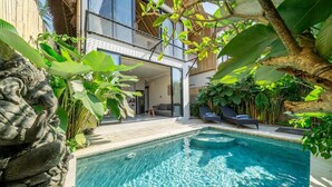 A swimming pool with a stone sculpture, surrounded by lush greenery and a modern house with a balcony. - Brand NEW 1BR Villa+Huge Pool+Jungle View+Top Spot (Gianyar Regency)