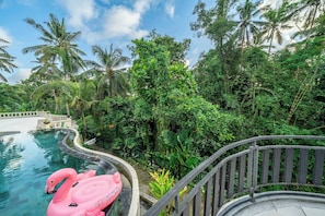 A pool with a curving edge, surrounded by lush greenery and palm trees.