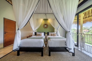 A double room with two beds, each with a canopy, a wooden door, a round mirror, and a view of the outdoors. - Designer Grand Suite in Ubud's Best Mesari Hotel (Gianyar Regency)
