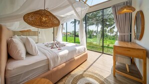 A bedroom with a large bed, a wooden bedside table, a mirror, and a view of a lush landscape through large windows. - Cozy 1BR in Ubud's Heart w Large Pool+Jungle View3 (Tampaksiring)