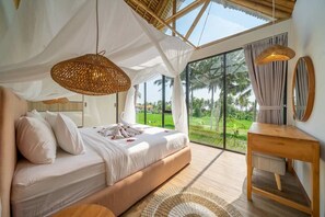 A bedroom with a large bed, a wooden bedside table, a mirror, and a view of a lush landscape through large windows. - Cozy 1BR in Ubud's Heart w Large Pool+Jungle View3 (Tampaksiring)