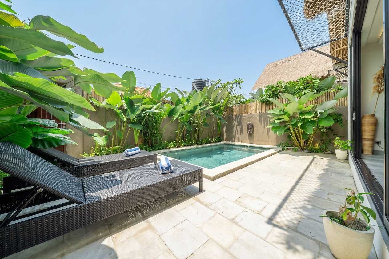 Ein privater Poolbereich mit Liegestühlen, umgeben von tropischen Pflanzen und einer Struktur mit Reetdach.