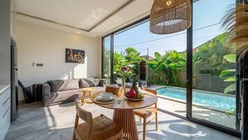 Ein modernes Wohnzimmer mit Essbereich, großem Fenster und Blick auf einen Pool.