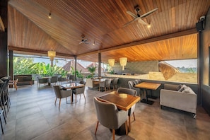Un espace intérieur vaste et lumineux, avec un plafond en bois, de nombreux espaces de détente comprenant des tables et des chaises, et une vue sur l’extérieur.