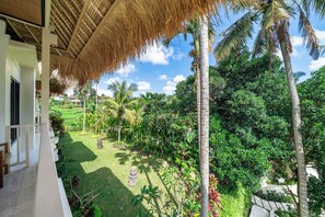 A tropical garden with palm trees and a thatched roof structure. - Designer Ricefield View Suite in Mesari Hotel Ubud (Gianyar Regency)