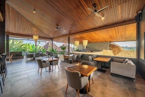A spacious indoor area with wooden ceiling, multiple seating arrangements including tables and chairs, and a view of the outside. - Serene Stylish Room in Cozy Mesari Hotel Ubud (Gianyar Regency)
