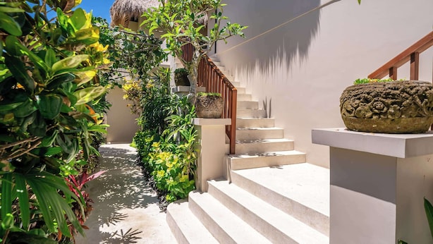 A staircase leading up to a building with a thatched roof, surrounded by lush greenery and a clear sky.