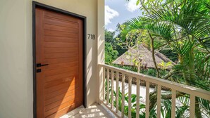 A wooden door with the number 718, a balcony with a white railing, and tropical vegetation.