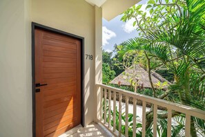 A wooden door with the number 718, a balcony with a white railing, and tropical vegetation.