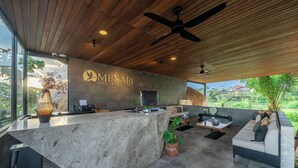 Un espace d’accueil doté d’un plafond en bois, d’un comptoir de réception, d’un canapé et offrant une vue sur la verdure environnante.
