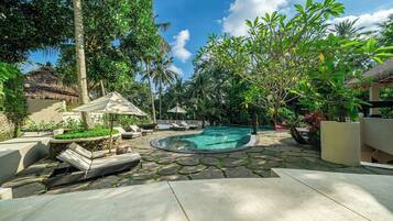 A pool area with lounge chairs and umbrellas, surrounded by tropical vegetation.