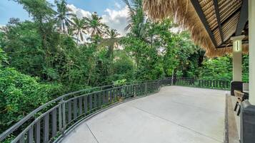 A curved pathway with a metal railing, surrounded by dense tropical vegetation and palm trees.
