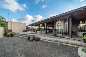 Un edificio moderno con un área de estar al aire libre techada, muros de piedra y plantas en macetas.
