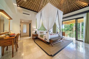 Un dormitorio amplio con una cama grande, una sala de estar con mesa y sillas, y un balcón con vistas a la vegetación.