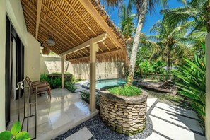 A poolside area with a stone planter, lounge chairs, and a thatched roof structure. - Boho Serene 1BR Villa w Pool & Garden in Lush Ubud (Gianyar Regency)