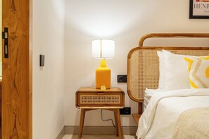 A neatly made bed with a white and yellow pillow, a small wooden nightstand with a yellow lamp, and a wicker headboard. - Stylish Flat with Kitchen in Peaceful Part of Ubud (Gianyar Regency)