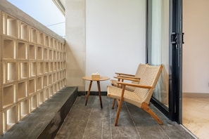 A balcony with a woven chair and a small round table, a tiled floor, and a glass door. - Stylish Flat with Kitchen in Peaceful Part of Ubud (Gianyar Regency)