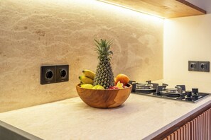 Een keukenblad met een houten kom met fruit en een ananas, een gasfornuis en stopcontacten aan de muur.