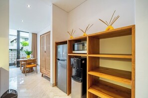 A modern kitchen with a refrigerator, microwave, and water dispenser, wooden shelves, and a dining area with a table and chairs. - Stylish Flat with Kitchen in Peaceful Part of Ubud (Gianyar Regency)