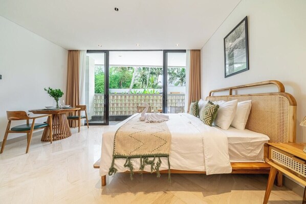 A bedroom with a bed, a desk, and a chair. There is a balcony with a view of trees. - Cozy 1BR in Serene Ubud - Kitchen, Balcony, Pool (Gianyar Regency)