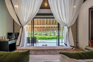 A bedroom with a bed, curtains, a TV, and a view of a pool and garden. - Designer 1BR Villa in Serene Ubud - Pool + Garden (Gianyar Regency)