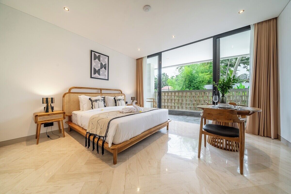 A spacious bedroom with a large bed, a bedside table, a chair, and a view of the outdoors.