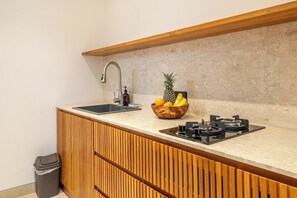 Eine Küche mit einem Holzkasten, einem Spülbecken, einer Obstschale und einem Gaskochfeld.