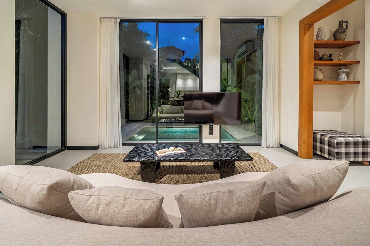 Ein modernes Wohnzimmer mit einer Couch, einem Couchtisch und Blick auf einen Pool durch Glastüren.