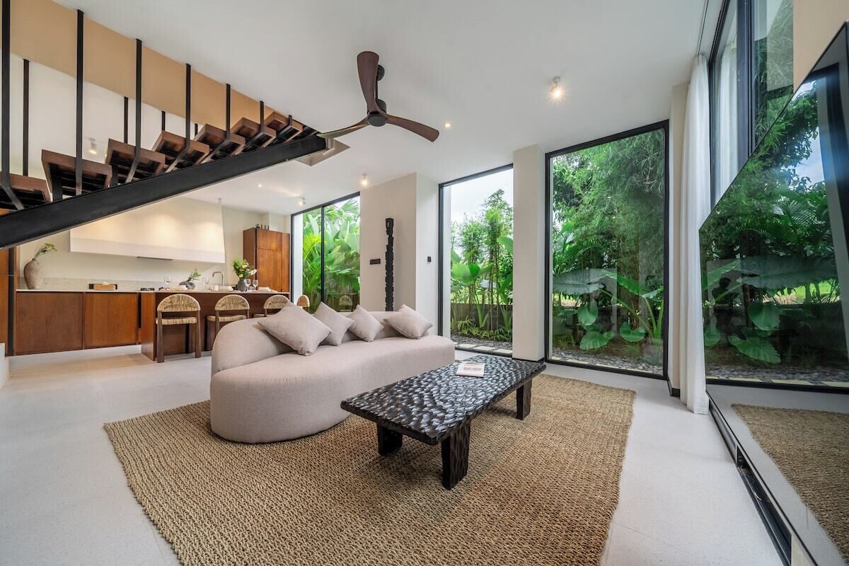 Ein moderner Wohnraum mit Treppe, einer Couch, einem Couchtisch und großen Fenstern mit Blick auf Grünflächen.