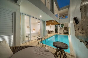 A poolside area with a lounge chair, a small table, and a staircase leading to an upper level. - Casa Sud Villa - Modern 3BR w Pool, Outdoor Lounge & Beach Access (Kabupaten Badung)