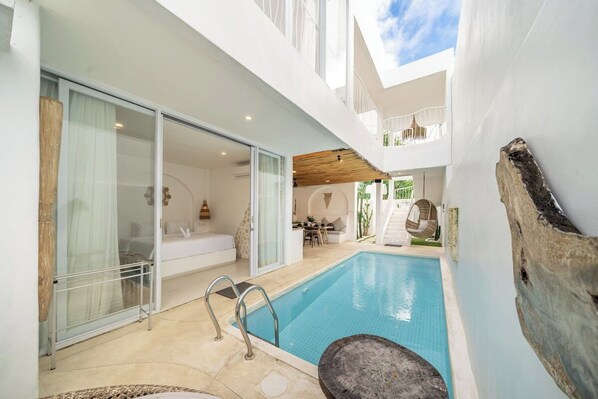 A modern outdoor swimming pool area with a glass door leading to a bedroom, a wooden deck, and a stone feature. - Casa Sud Villa - Modern 3BR w Pool, Outdoor Lounge & Beach Access (Kabupaten Badung)